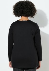 Czarna koszula z długim rękawem wykonana z miękkiej tkaniny, z okrągłym dekoltem, o luźnym kroju i nieco wydłużonym tylnym obszyciu.