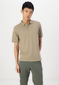 Polo shirt à manches courtes en khaki en coton, avec un col classique, une patte de boutonnage à trois boutons et un petit logo sur la poitrine.