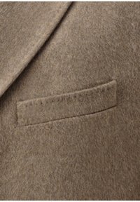Brauner Wollblazer-Detail mit strukturierter Oberfläche und einer einzelnen, vernähten Tasche auf der Brust, die saubere, gerade Kanten aufweist.