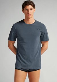 Šedé tričko s kulatým výstřihem vyrobené z bavlny, s krátkými rukávy a volným střihem. Hladký povrch, žádné vzory ani viditelné prvky.