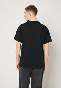 Black cotton T-shirt with short sleeves, crew neck, relaxed fit, and a smooth texture. Worn with dark gray jeans.