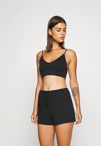 Czarny krótki top na cienkich ramiączkach z dekoltem w serek, w połączeniu z czarnymi szortami w małe białe kropki oraz regulowanym wiązaniem w pasie.