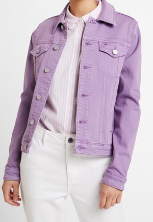 Frau trägt eine fliederfarbene Jeansjacke über einem rosa-weiß gestreiften Hemd mit Knöpfen und weiße Hose, dargestellt von den Schultern bis zur Hüfte.