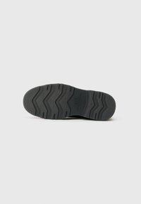 Semelle de chaussure en caoutchouc noir avec un motif de bande de roulement en zigzag, portant un nom de marque embossé et des bords lisses, conçue pour offrir adhérence et durabilité.