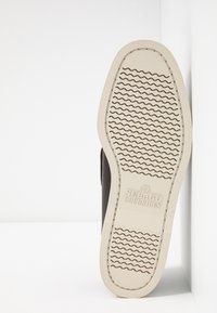 Brauner Lederbootsschuh mit einer weißen Gummisohle, die ein wellenförmiges Profilmuster und ein geprägtes Logo zeigt. Die Seitenansicht hebt die Form des Schuhs hervor.