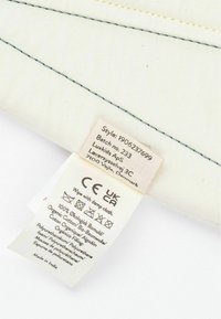 Organic cotton label on a beige fabric, with blue stitching. Contains care instructions and product details in multiple languages.