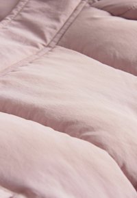 Lyserød, puffy dyne med en blød, glat tekstur og quiltede detaljer, der har et diagonalt søm mønster og et let design.