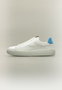 Λευκό sneaker χαμηλού προφίλ με μπλε ταμπελάκι στη φτέρνα, μπροστινό δέσιμο με κορδόνια και ανάγλυφο γεωμετρικό σχέδιο στη χοντρή σόλα, εμφανίζεται σε πλευρικό προφίλ.