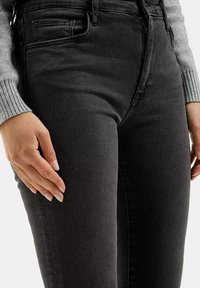 Czarne jeansy o wysokim stanie z gładką fakturą, z przednią kieszenią i subtelnymi detalami przeszycia, w połączeniu z szarym swetrem w prążki.