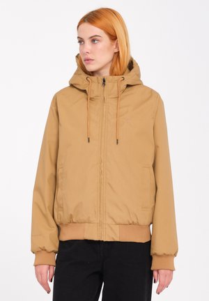 Veste à capuche beige avec une fermeture éclair à l'avant, des poignets élastiques et un ourlet ajusté. Elle présente deux poches latérales et un logo discret sur la poitrine.