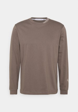 T-shirt manches longues taupe à col rond avec logo Calvin Klein Jeans sur le col et petit logo CK sur le poignet de la manche gauche.
