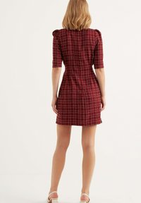 Röd klänning med rutmönster, korta puffärmar, smal midja och vid kjol. Tillverkad i bomullsblandning med en ren finish.