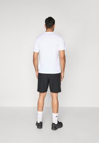 Weißes Feuchtigkeitsregulierendes T-Shirt, schwarze Shorts, weiße Socken mit schwarzen Streifen und schwarze Sportschuhe. Schlichte, funktionale Sportkleidung.
