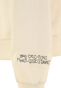 Cremfarbener Sweatshirt mit gerippten Bündchen und besticktem Text am Ärmel, der lautet: "SCHLECHTE ENTSCHLÜSSE MACHEN GUTE GESCHICHTEN."