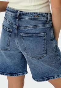 Shorts in denim con gradiente da blu chiaro a blu scuro, dotati di tasche posteriori, una vita con un sottile simbolo dell'infinito e un orlo sfrangiato.