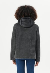 Harmaa fleece-takki mustalla, päälystetyllä hupulla. Teksturoitu kangas, pitkät hihat ja suora helma; soveltuu rentoon käyttöön.