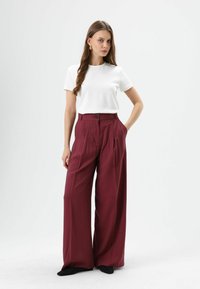 Wit T-shirt met korte mouwen gecombineerd met wijde, hooggetailleerde bordeauxrode broek met knopen aan de voorkant en zijzakken. Glad stofgevoel.