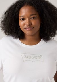 White cotton t-shirt featuring a sparkly logo in gray thread. Crew neck design with short sleeves. Smooth texture, minimalistic style.