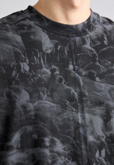 Camiseta de cuello redondo negro con un patrón abstracto gris texturizado. El material parece suave, con una superficie lisa y detalles de costura visibles.