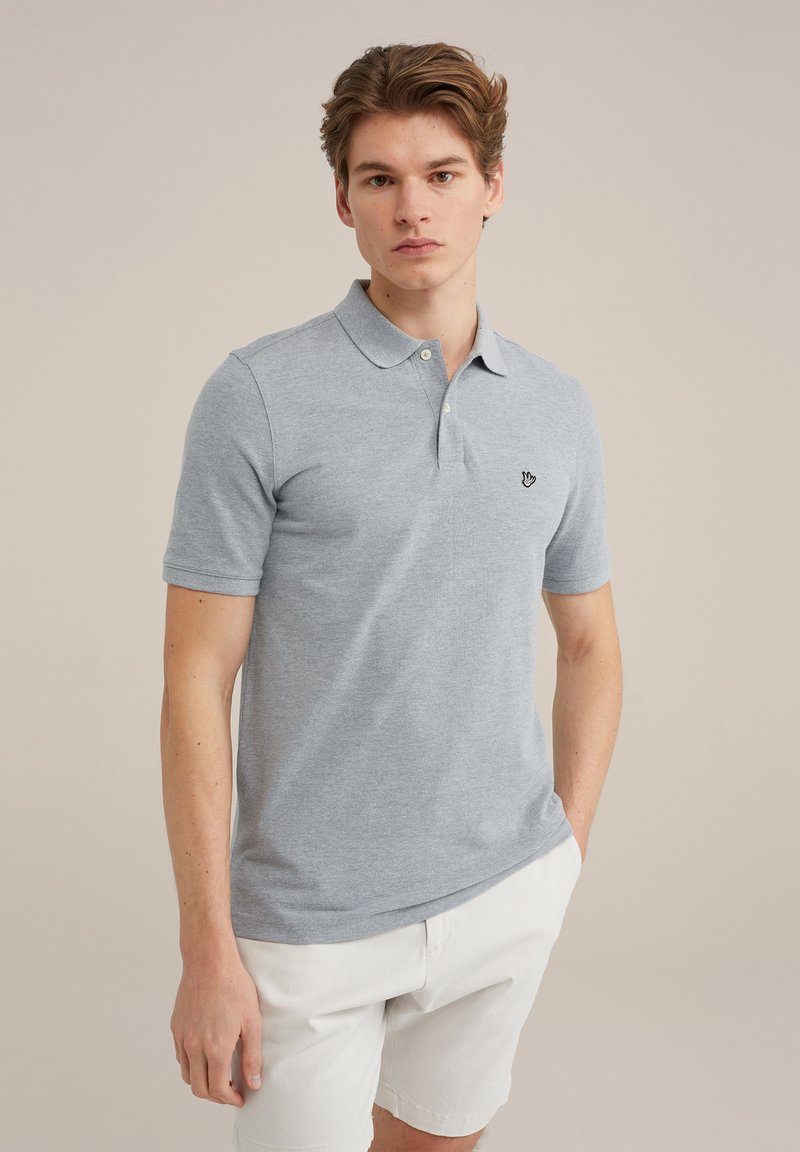 Gaiši pelēks polo krekls ar klasisku apkakli, īsām piedurknēm un izšūtu logotipu uz krūts, apvienots ar baltām šortiem.