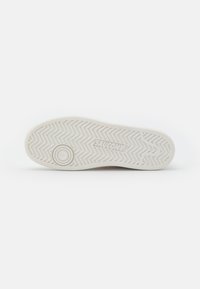 Suola di sneakers bianche in gomma con un motivo a spina di pesce, logo stampato nella parte centrale e un accento circolare vicino all'area delle dita.