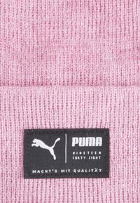 Ružová pletenina s textúrovaným povrchom. Obsahuje čiernu obdĺžnikovú nálepku s nápisom "PUMA" a logom skáčúcej mačky.