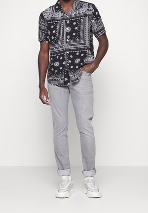 Korte mouwen zwart-wit gepatterneerd shirt met een kraag, gecombineerd met lichtgrijze slim-fit broek en witte sneakers.