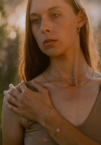 Ros�égoldene, geschichtete Halsketten mit feinen Ketten, getragen mit einem passenden Armband, das ein kreisförmiges Akzentstück aufweist, vor einem weichgezeichneten Hintergrund.
