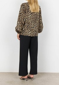 Blouse à imprimé léopard avec des manches bouffantes, associée à un pantalon noir large taille haute et des mules à imprimé animal. Texture de tissu douce.