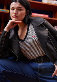 Giacca da biker in pelle nera, t-shirt a righe con scollatura a V e un piccolo logo rosso Levi's, jeans blu a vita alta e cintura nera strutturata.