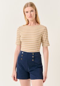 Beige geribbelde top met korte mouwen en witte strepen, gecombineerd met marineblauwe hoge taille shorts met gouden knoopaccenten.