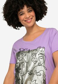 Lavendel t-shirt med abstrakte linjetegninger af ansigtet på en sølvmetalisk baggrund. Blød tekstur, scoop-udskæring, korte ærmer.
