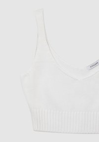 Bralette bianco lavorato a maglia con scollatura a V e banda larga a coste. Presenta spalline sottili e una texture liscia in tutta la sua superficie. Etichetta con la scritta "CALLIOPE."