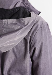 Světle fialová bunda s kapucí, vyrobená z texturované tkaniny, s meshovou podšívkou a viditelnými švy. Zapínání na zip vpředu.