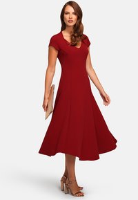 Red, cap-sleeve dress featuring a fitted bodice and flared skirt, made of smooth fabric. Paired with strappy heels and a clutch.