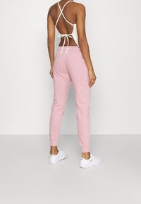 Ljusrosa joggers med slim fit, elastisk midja och muddar. Tillverkade av mjukt tyg; har sidofickor och en avslappnad design.