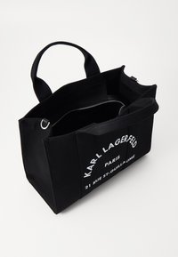 Svart lerret tote-veske med dual håndtak. Har hvit trykket logo og tekst. Innvendig har den en glidelåslomme og et romslig hovedrom.
