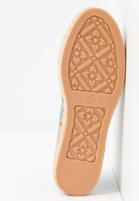 Semelle de chaussure en caoutchouc beige avec un motif floral, présentant un bord supérieur bleu clair. La semelle est texturée pour offrir une meilleure adhérence.