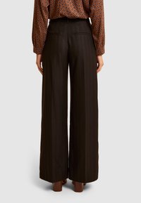 Spodnie o szerokich nogawkach w ciemnobrązowej tkaninie z delikatnym prążkiem. Charakteryzują się wysokim stanem i dopasowanym krojem oraz tylnymi kieszeniami. Noszone z wzorzystą bluzką.