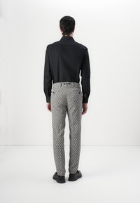 Black long-sleeve shirt and patterned gray trousers with white geometric design. Model wears black shoes, facing away against a plain background.