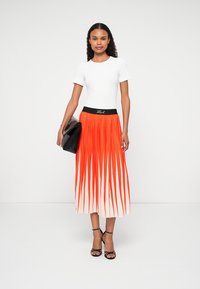 Fehér, testhezálló póló, amelyet egy hosszú, redőzött narancs-fehér színátmenetes szoknyával párosítottak. Fekete derékpánt logó részlettel. Fekete kézitáska és szandál.