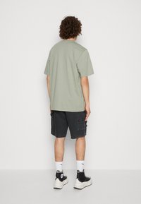 Lichtgroen katoenen t-shirt, relaxte pasvorm, gedragen met zwarte cargoshorts en zwarte hoge sneakers. Witte sport sokken complementeren de outfit.