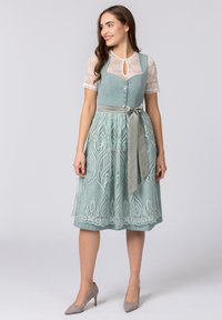 Ein türkisfarbenes Kleid mit Spitzenschößen, einem taillierten Oberteil und einem A-Linien-Rock, der mit aufwendigen gestickten Mustern und einem Satinband verziert ist.
