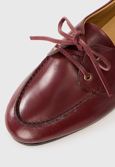 Burgundy leather loafers with a rounded toe, lace-up design, gold eyelets, and contrasting stitching details. Smooth texture with shiny finish.