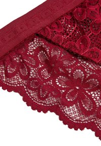 Burgunderfarbenes Spitzegewebe mit floralen Mustern und gewellten Rändern, kombiniert mit einem strukturierten weinrotfarbenen Band an der Oberseite. Feingliedriges Design.