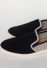 Zwarte geperforeerde instapschoenen met lichtgrijze accenten en een witte rubberen zool, met een combinatie van glad en textuur materiaal.