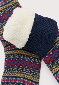 Des chaussettes tricotées présentent un motif géométrique en bleu, rouge et vert ; une épaisse bordure côtelée marine avec une douce doublure beige et duveteuse en haut.
