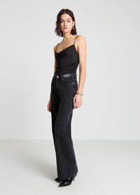 Body noir à col bénitier avec fines bretelles, associé à un jean noir taille haute à jambes larges, orné d'une ceinture chaîne argentée, et des escarpins noirs pointus.