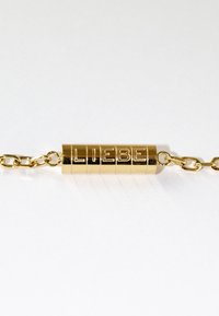Bracelet en or avec un charm cylindrique gravé du mot "LIEBE". La chaîne est composée de maillons et d'un design de fermoir unique.