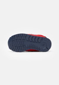 Chaussure de sport rouge avec une semelle en caoutchouc texturé présentant un motif en vagues, des accents bleus et une tige en mesh pour la respirabilité.